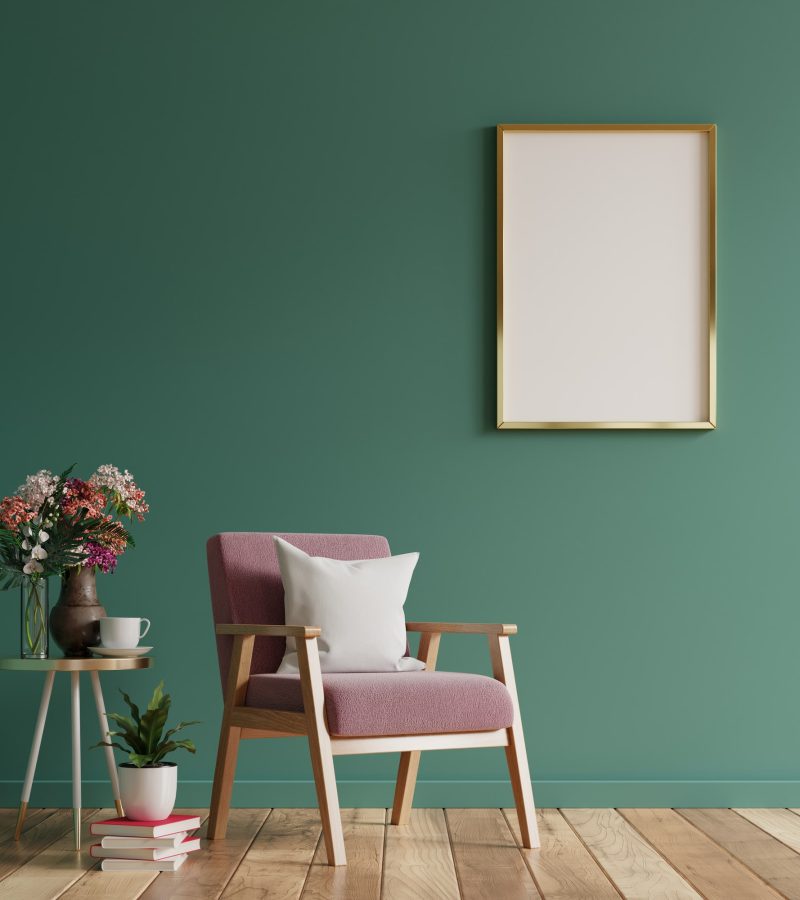 Modern Living Room with Green Wall, Pink Armchair, and Stylish Decor cozy modern living room with a green wall, a pink armchair with a pillow, a small side table with plants and flowers, and a blank gold-framed picture
