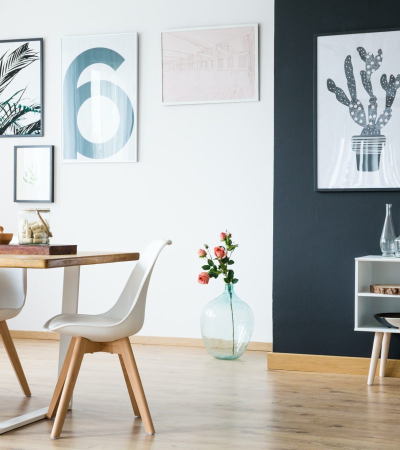 Stylish Dining Room with White Chairs, Wooden Table, and Framed Artworks modern dining room featuring a wooden table, white chairs, decorative flower vases, and framed artwork on the wall with a black accent corner.